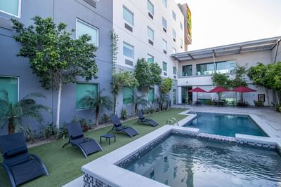 Outdoor pool with black lounge chairs by tropical trees at Hotel Mirra, best hotel in San Luis Rio Colorado for work trips