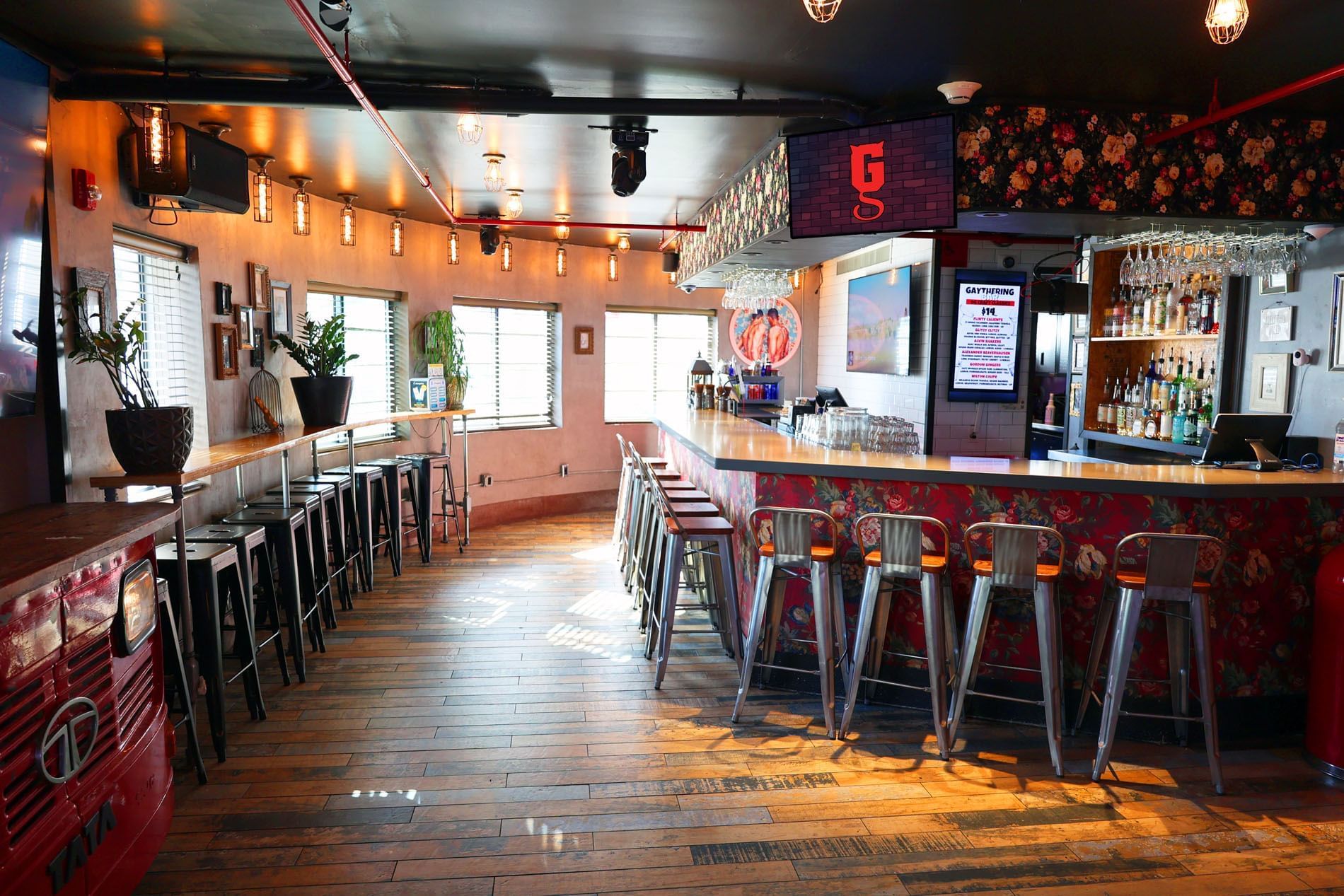 A wide view of a bar with stools, a counter, and decorative lighting.