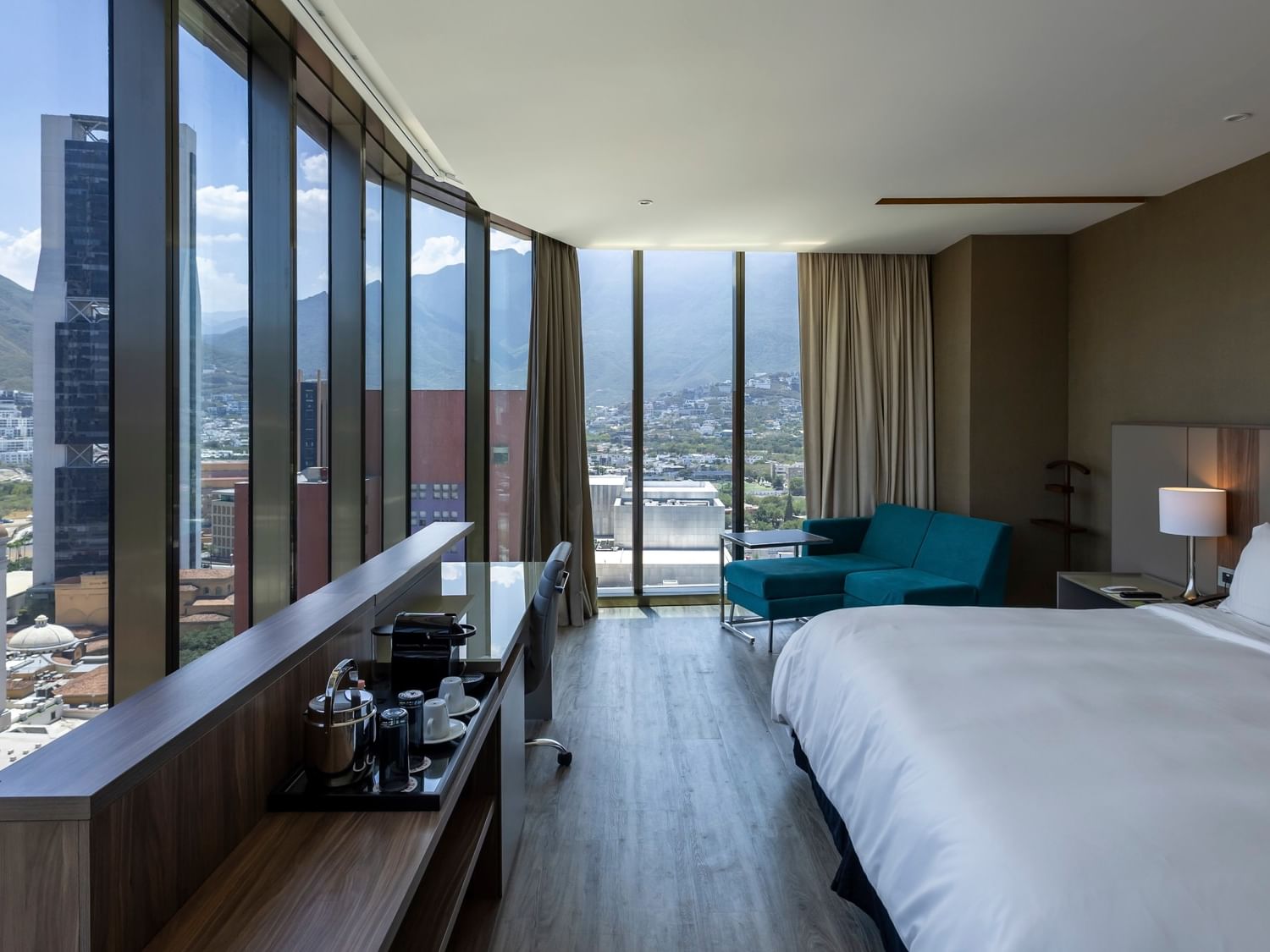 Junior Suite con cama king, sofá turquesa y ventanales con vista panorámica en Camino Real Fashion Drive Monterrey