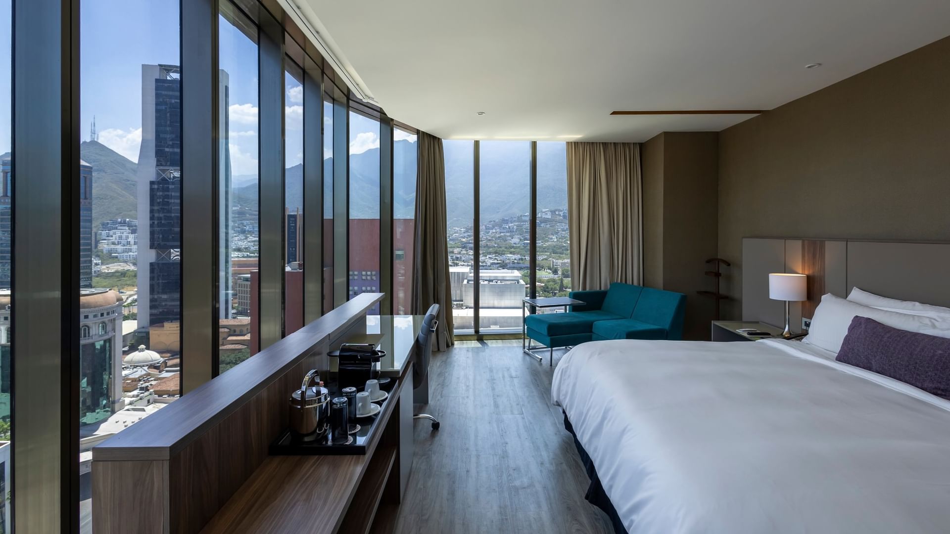 Junior Suite con cama king, sofá turquesa y ventanales con vista panorámica en Camino Real Fashion Drive Monterrey