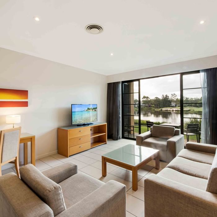 Two Bedroom Apartment living room with sofas, TV, and garden view through sliding doors at Mercure Kooindah Waters