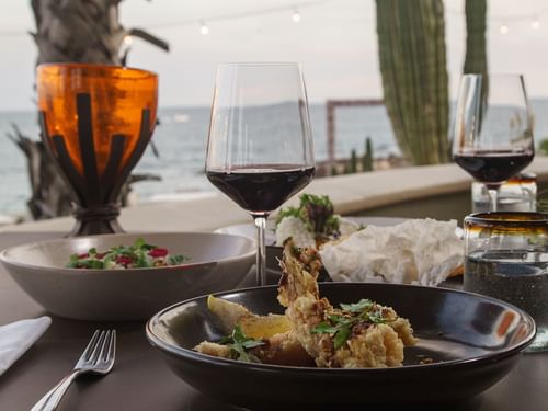 Plato de mariscos y copas de vino en una mesa con vista al mar en el restaurante Pitahayas en Hacienda Del Mar Los Cabos.