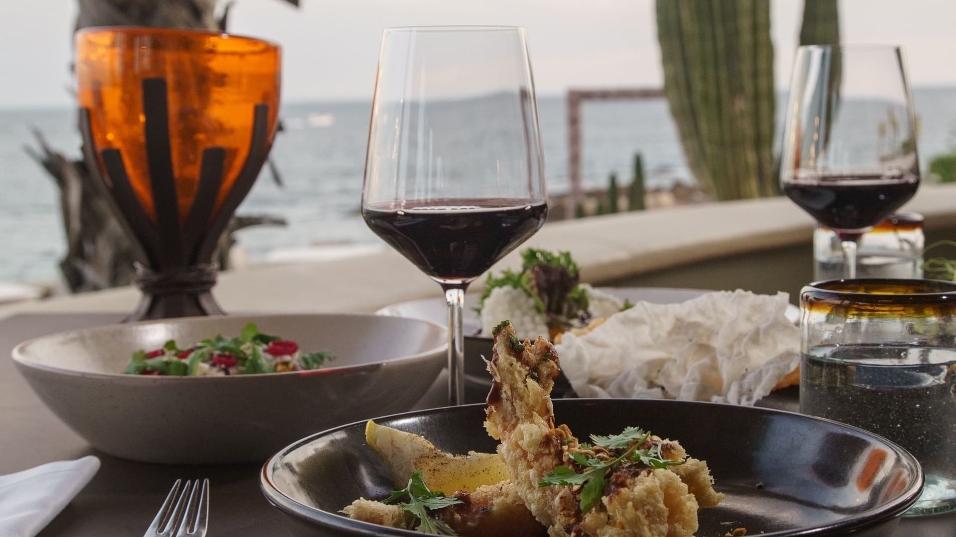 Plato de mariscos y copas de vino en una mesa con vista al mar en el restaurante Pitahayas en Hacienda Del Mar Los Cabos.