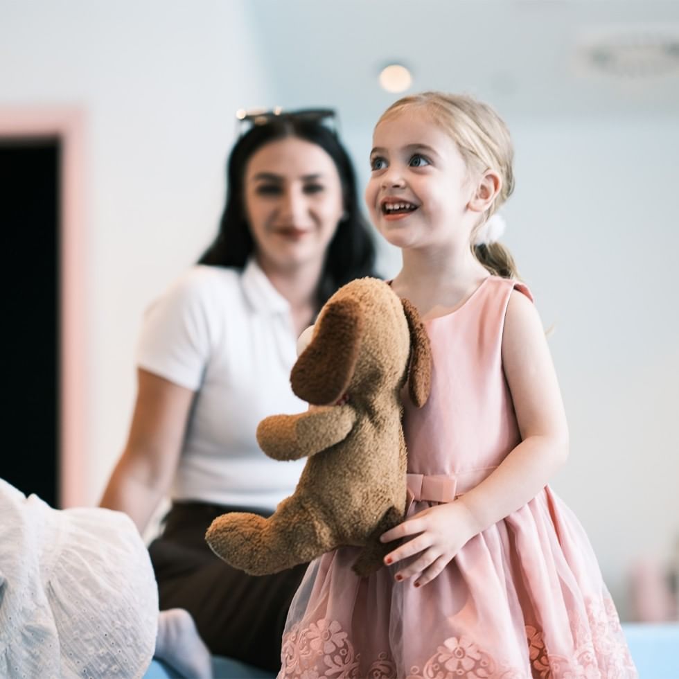 Smiling child holding teddy bear with woman at Puppet Theatre with Christian Mair.