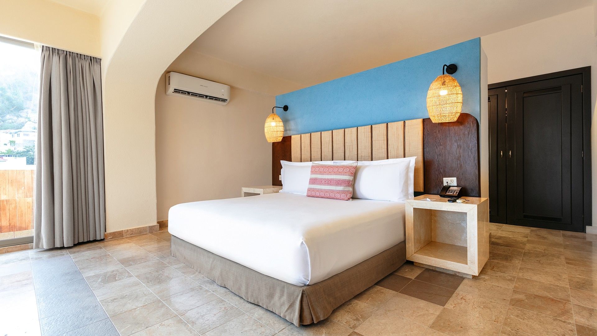 King Master Suite bed with a blue accent wall, wicker lamps, and marble bedside furniture at Camino Real Acapulco Diamante