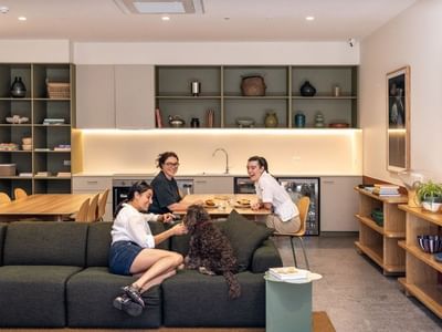 Three residents and a dog relax in a modern communal lounge with kitchen, dining area, and contemporary decor at Swift Walk