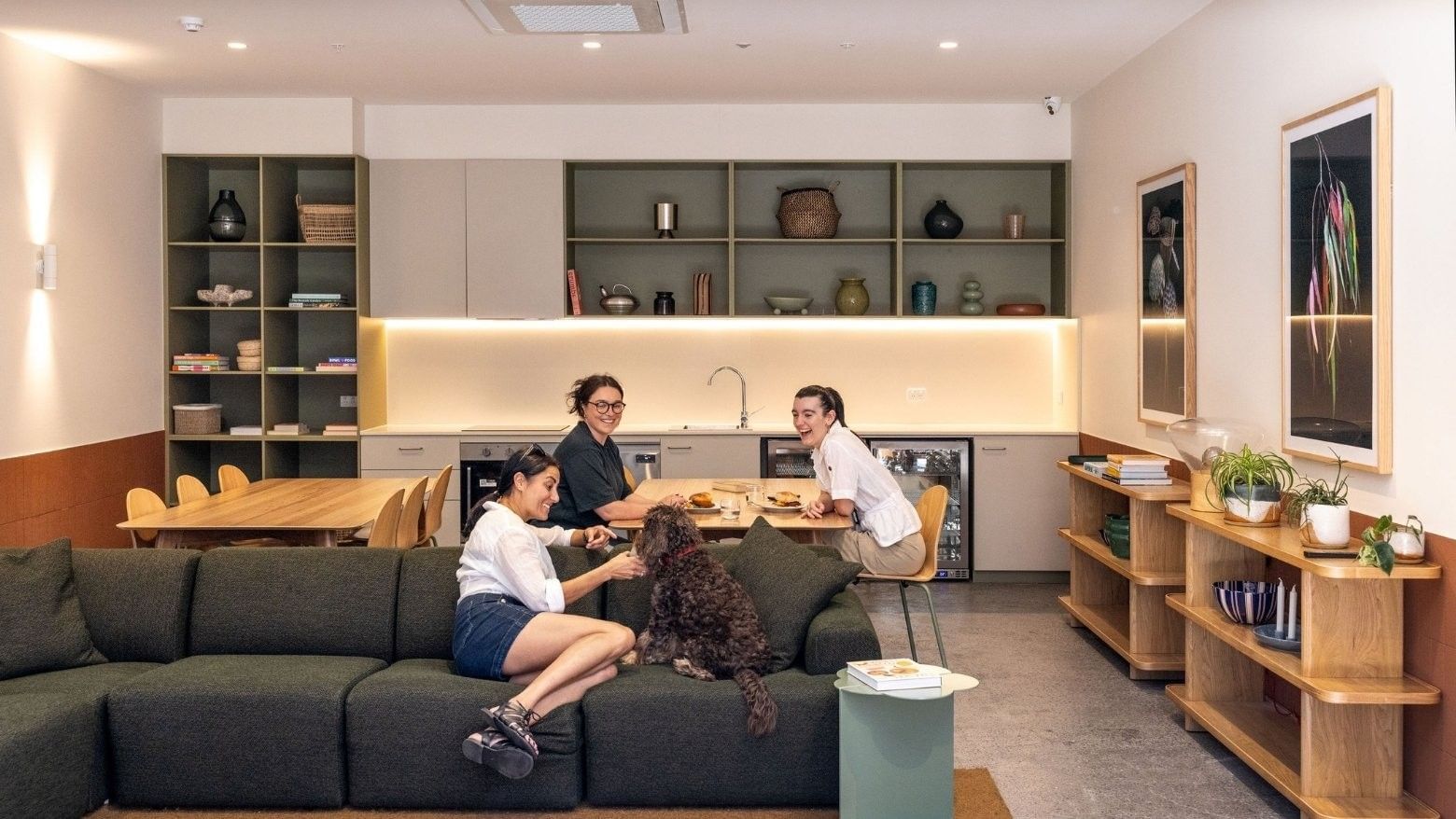 Three residents and a dog relax in a modern communal lounge with kitchen, dining area, and contemporary decor at Swift Walk