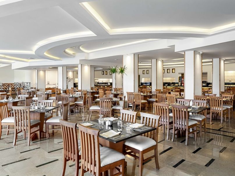 Elegantes Restaurant mit vielen Tischen und Stühlen, hellen Decken und großen Säulen im Hintergrund.