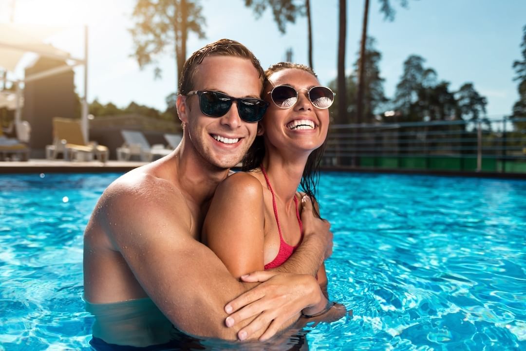 A couple embracing in a swimming pool, surrounded by sunlight and palm trees at Cove Pocono Resorts