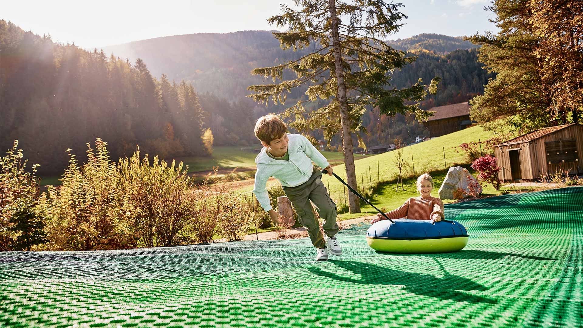 Bambino che aiuta bambina su un tubo gonfiabile in un parco giochi all'aperto in montagna.