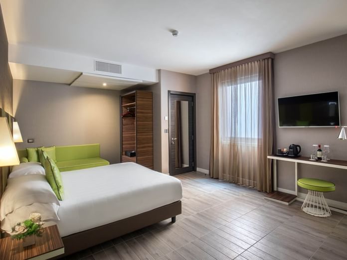 Large Family Room featuring a queen bed, seating area, wooden closet, TV, and desk with refreshments at The Republic Hotel