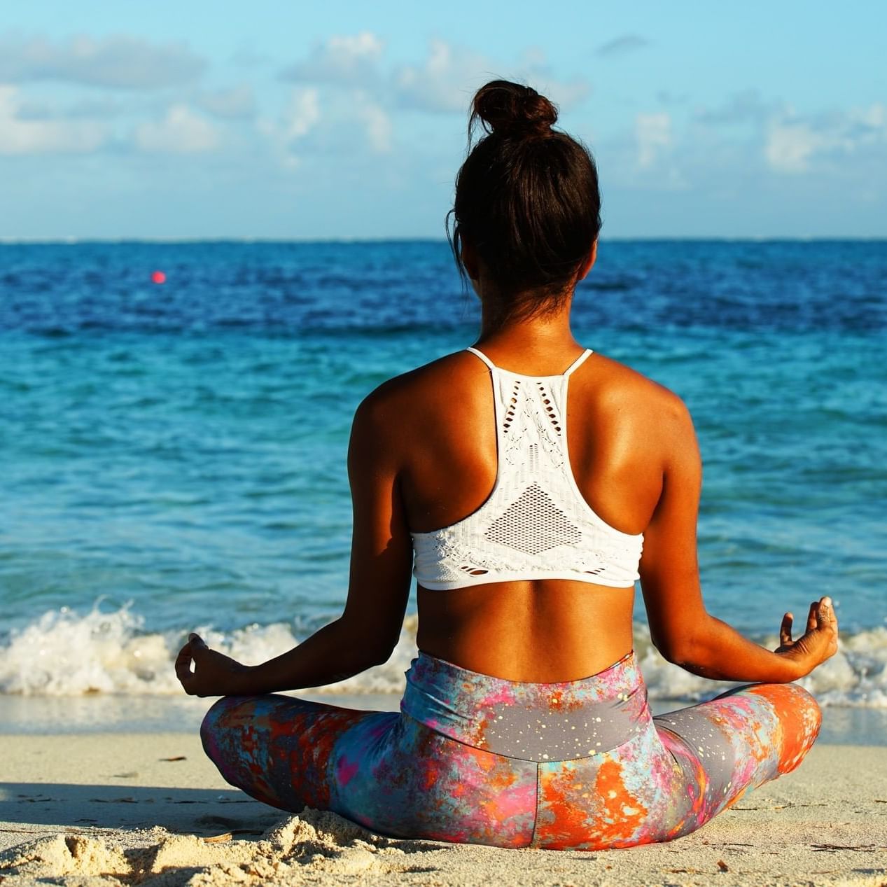 Woman meditating on the beach, seated and facing the ocean and sky near Windsong Resort On The Reef