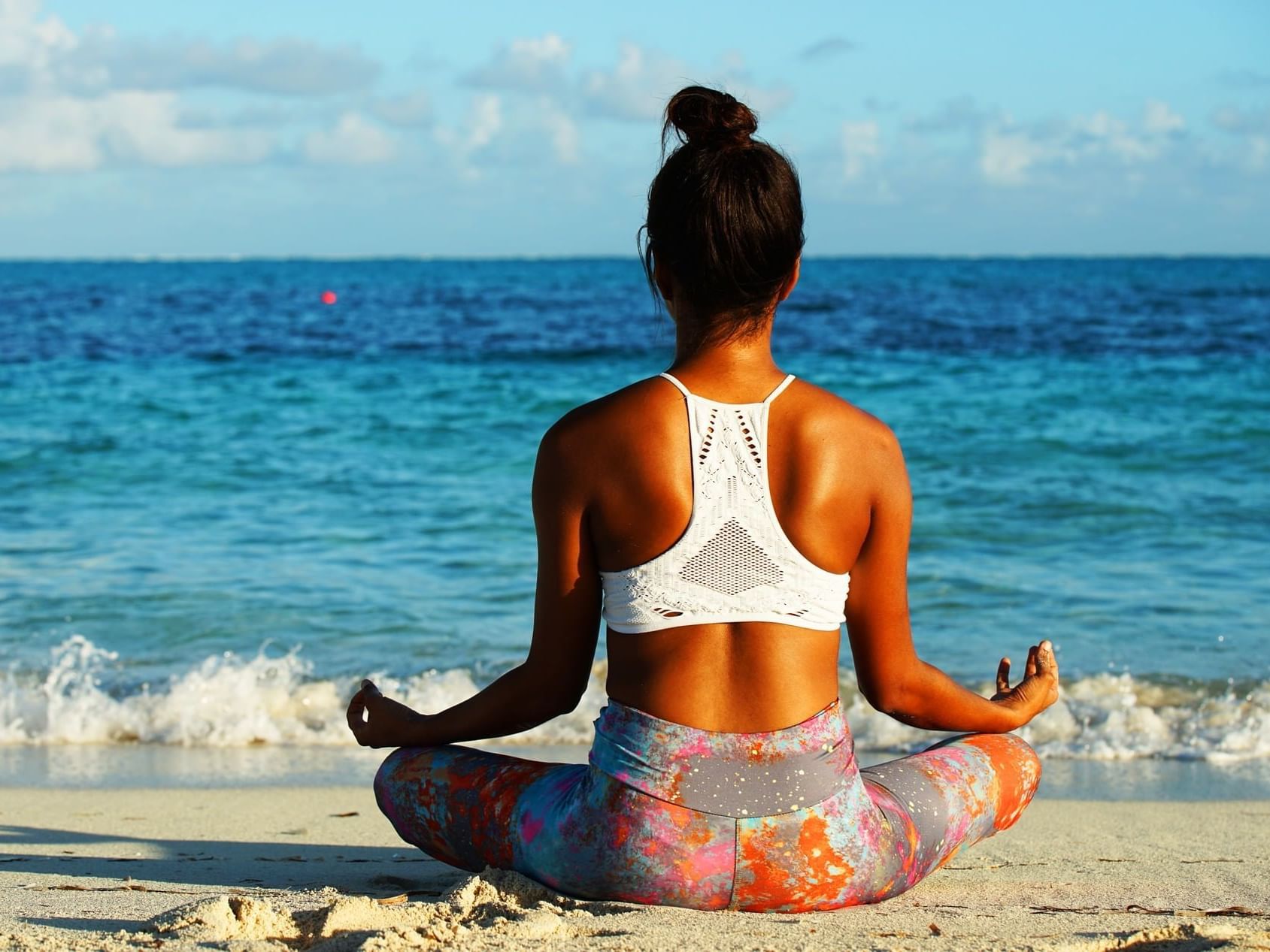 A woman sits cross-legged on the beach, meditating by the calm ocean near Windsong Resort On The Reef