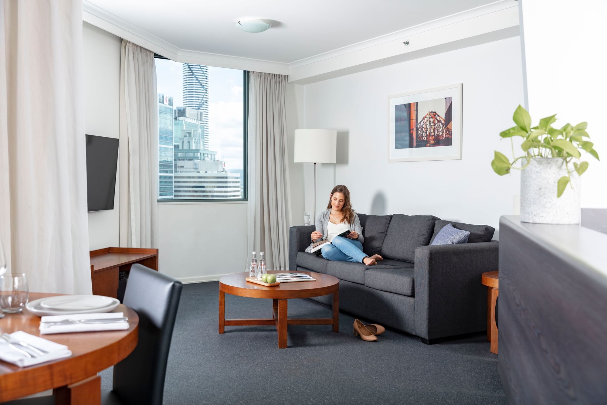 Woman reading a book on a dark sofa in Premium One Bedroom Apartments with a window view at The Sebel Brisbane