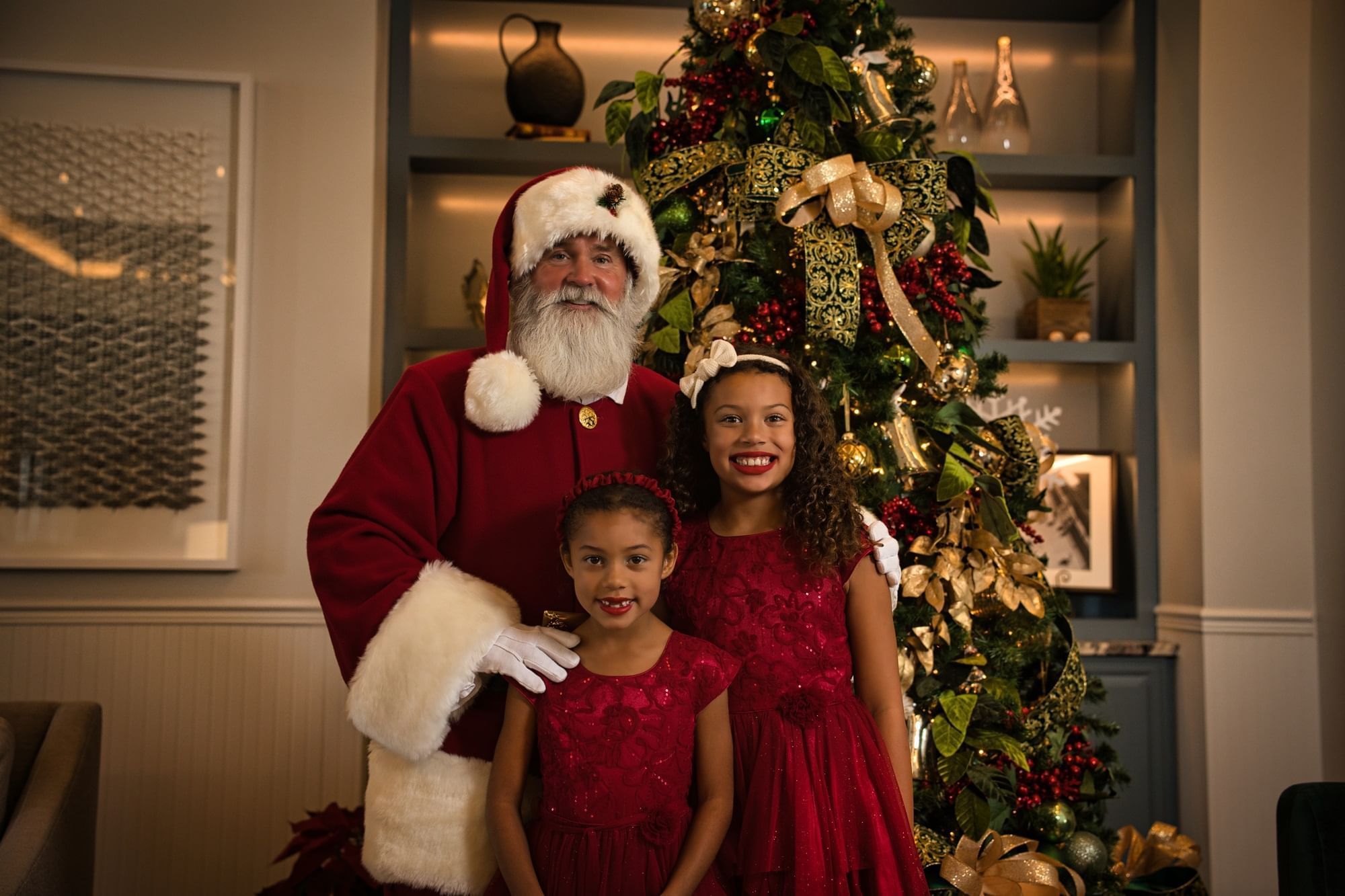 Santa Claus and two young girls posing in front of a decorated Christmas tree.