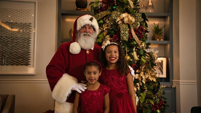 Two girls pose with Santa Claus in front of the Christmas tree at Camp Creek Inn.