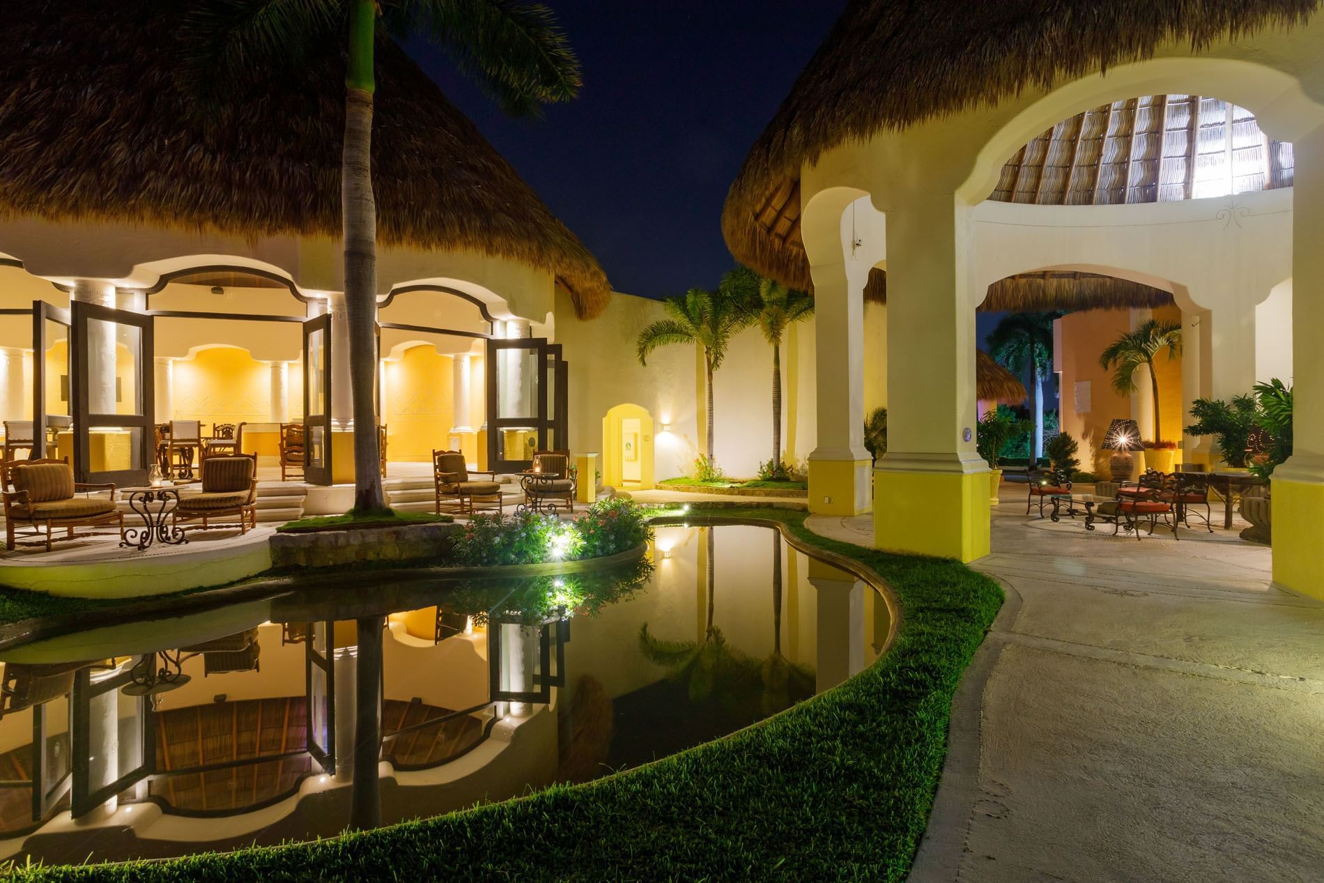 Stunning night view showing illuminated palapa villas reflected in a calm pool at Quinta Real Acapulco