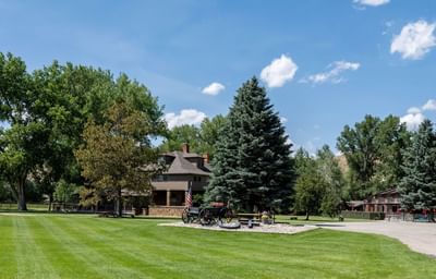Expansive green lawn at The Ranch at Ucross with a historic wagon, lodge building and towering trees
