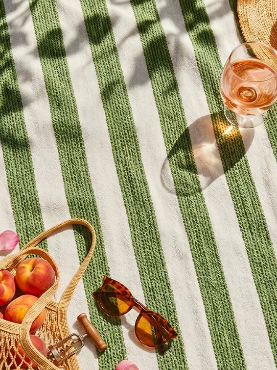 Serviette rayée verte et blanche avec chapeau de paille, lunettes de soleil, sac en toile et panier de fruits frais.