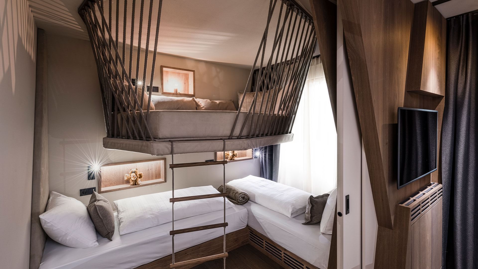 A loft bedroom with two beds below and one above, accessed by a wooden ladder.