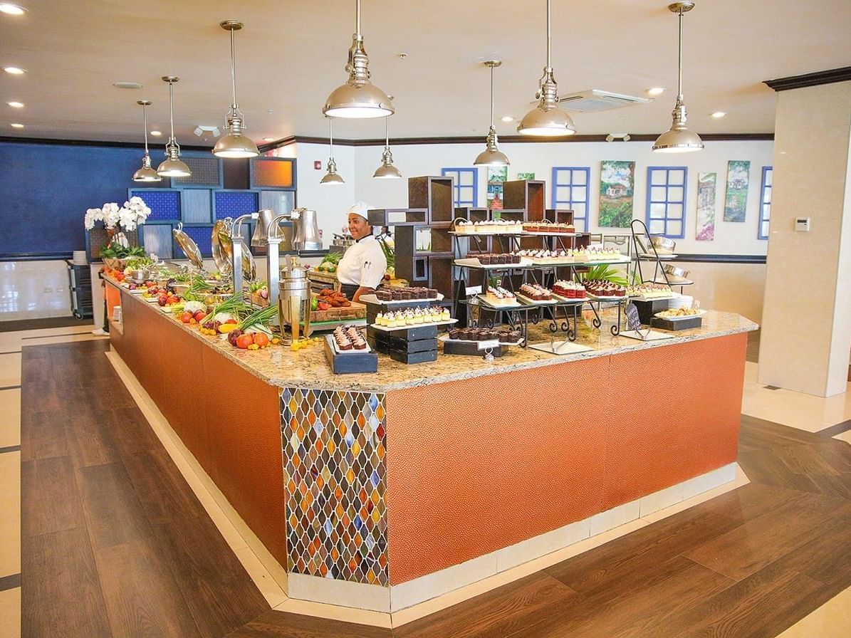 Chef standing behind a marble buffet display with pastries and salads under pendant lights at Jamaica Pegasus Hotel