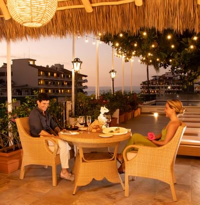 Couple enjoying a romantic candlelit dinner beneath a thatched terrace at sunset in Casa Dona Susana