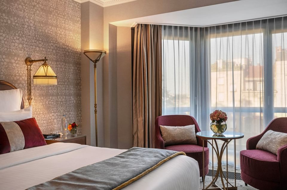 Red armchairs surrounding a glass table with flower vase and beside bed in Deluxe Room at Hotel Barsey by Warwick