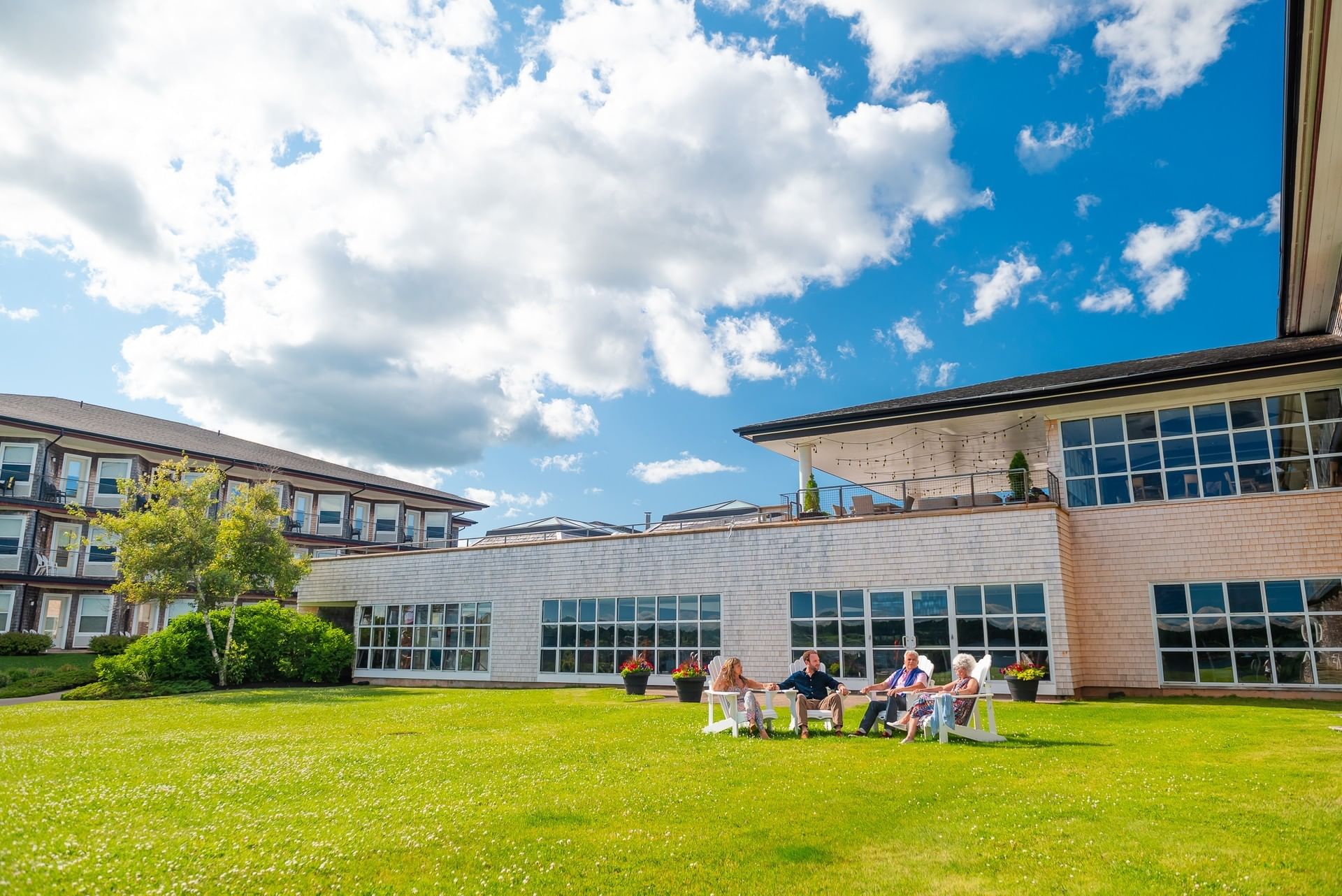 Guests relaxing in white chairs on a lawn surrounding building structures under a blue sky at Rodd Brudenell River Resort