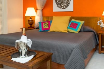 Champagne bottle and glasses on a wooden tray by a bed with colorful pillows in Executive Suite at Hotel Montana Haiti