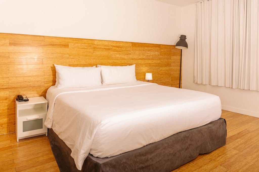 A wide view of a hotel room with a king-sized bed, wood paneling, and white linens.