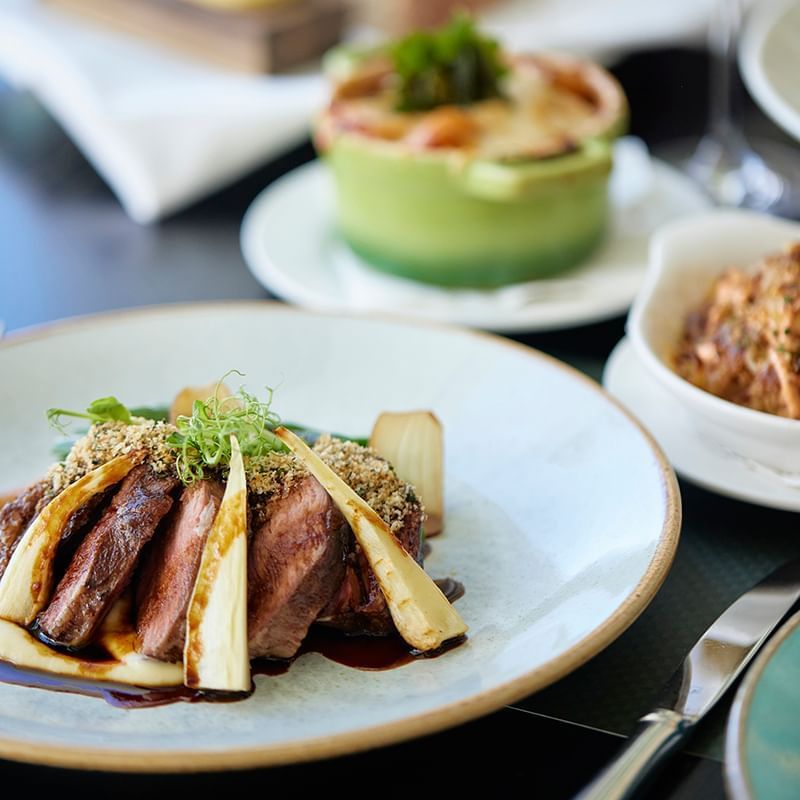 Sliced steak plated with garnish alongside two side dishes on table in Bistro Guillaume at  Crown hotels Perth