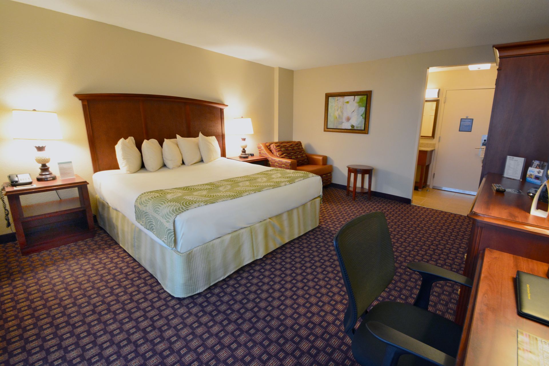 A wide-angle view of a hotel room with a king-sized bed, desk, chair, and nightstands.