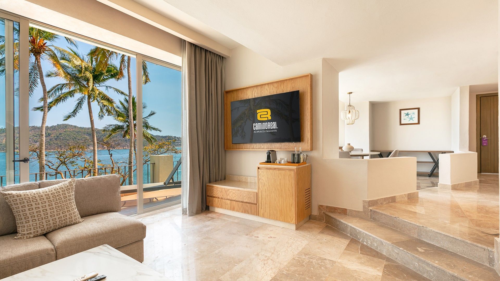 King Junior Suite featuring a sea view through glass doors and a wooden media console at Camino Real Acapulco Diamante
