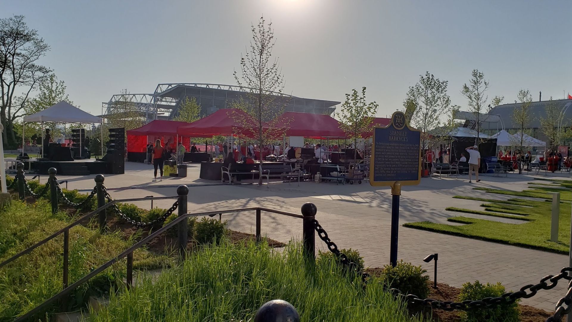 Red canopy tents set up by a stage and picnic tables, near a historic plaque and green lawn at Hotel X Toronto