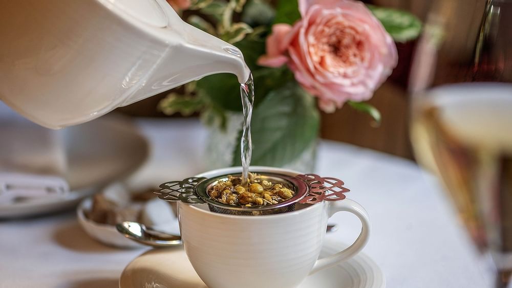 Tea being poured into a cup with a strainer at The Capital Hotel, Apartments & Townhouse London.