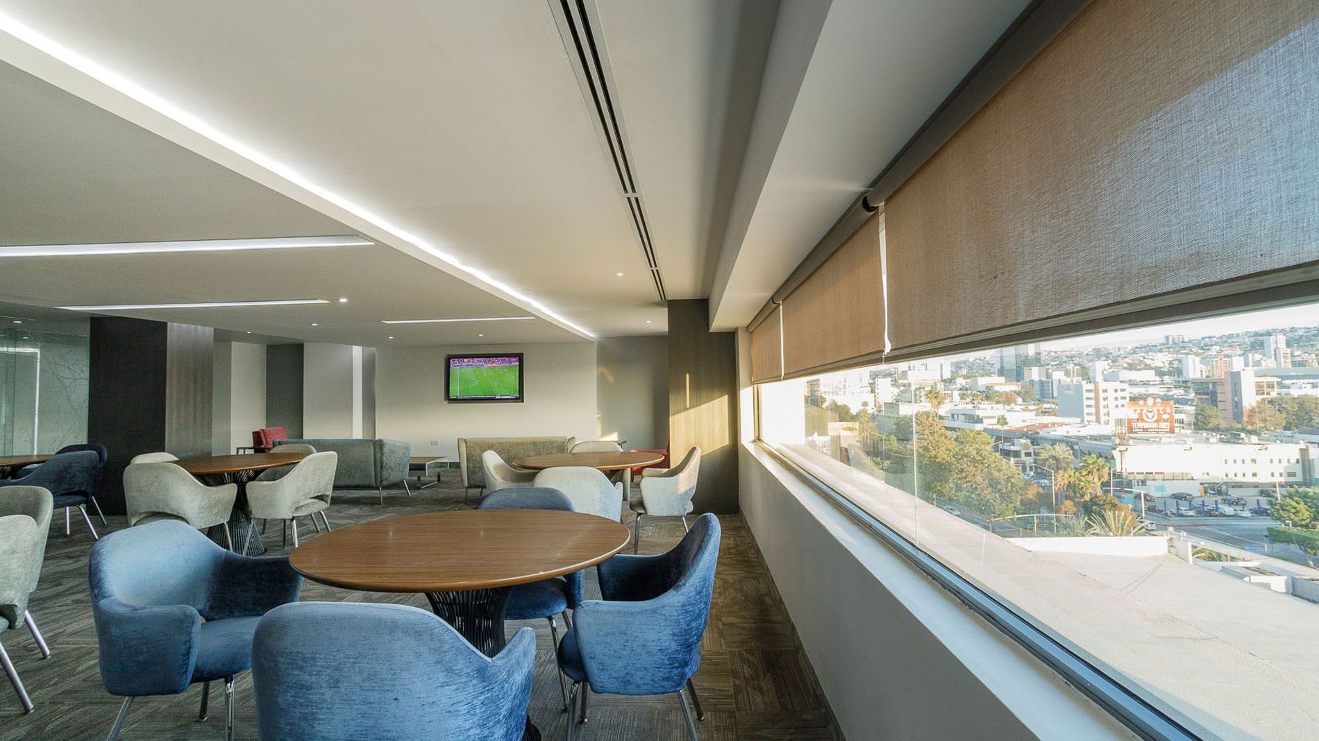 Modern lounge area with blue velvet chairs, round tables, and a panoramic city view window at Real Inn Tijuana