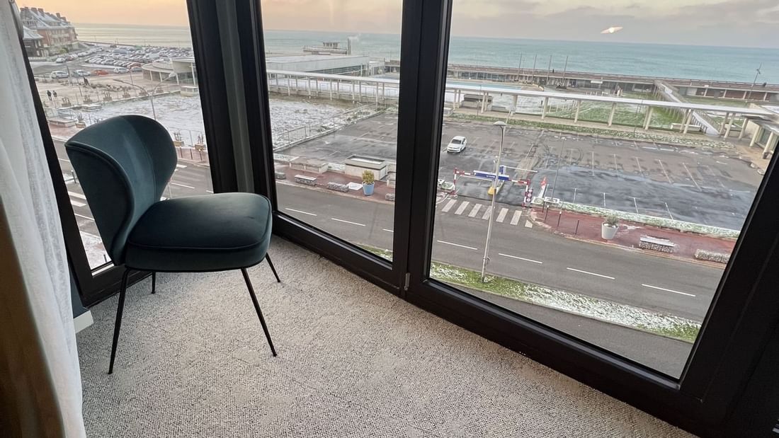 Vue d'une chaise devant une grande fenêtre avec vue sur un parking et l'océan.