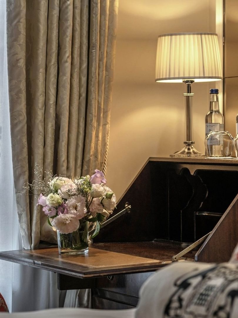Flower bouquet on a writing desk by a lamp, water bottles, & a armchair in Superior Single Room at Hotel Westminster Paris