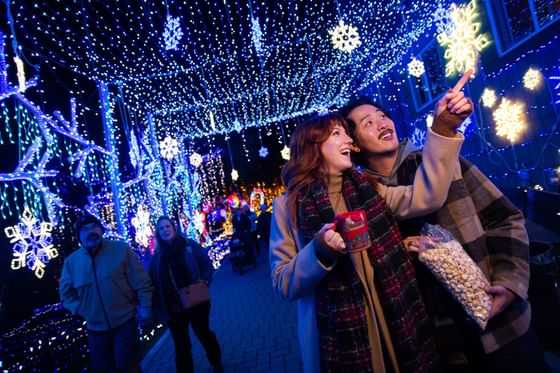 Couple enjoying festive holiday lights and snowflake decorations with hot beverages at Cambria Pines Lodge