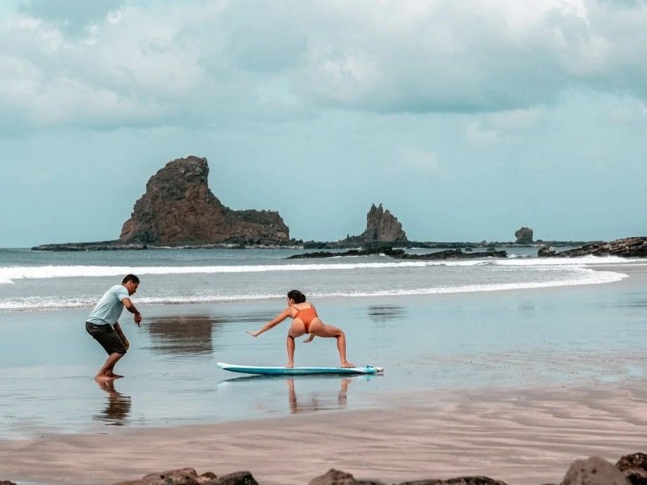 Woman on a surfboard by the shore under a cloudy sky near Morgan's Rock Reserve & Ecolodge