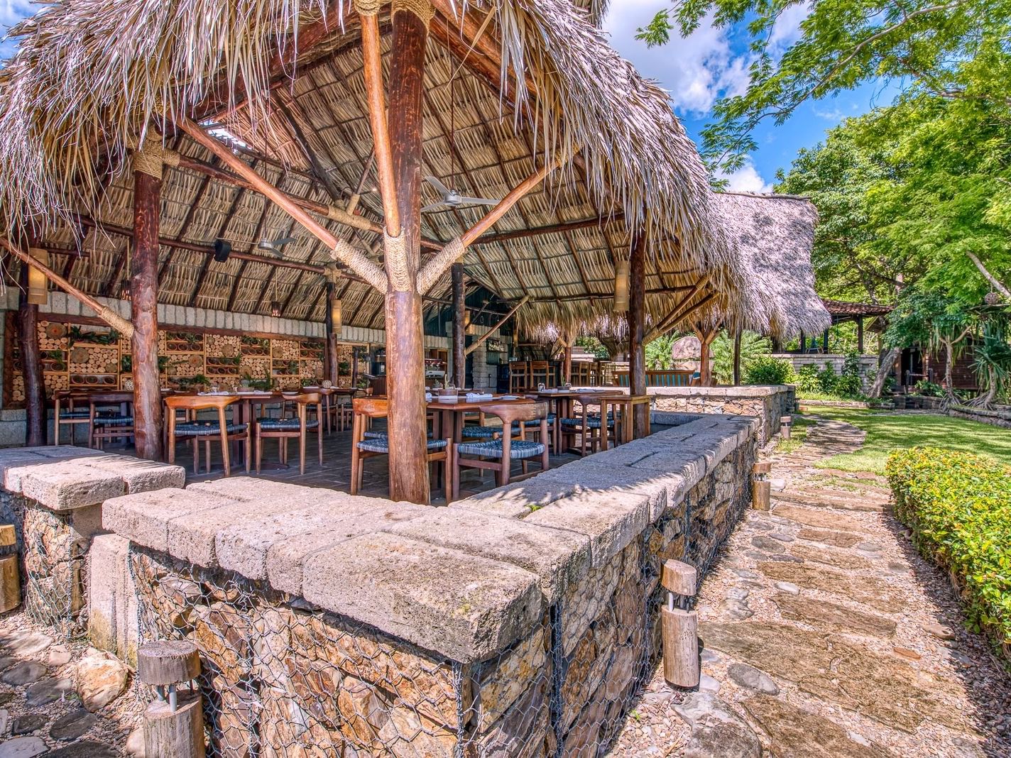Wood dining tables under a large thatched roof pavilion in La Bastide Restaurant at Morgan's Rock Reserve & Ecolodge