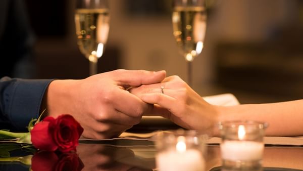 A man and woman holding hands, with a rose and champagne glasses on a table at Warwick Denver