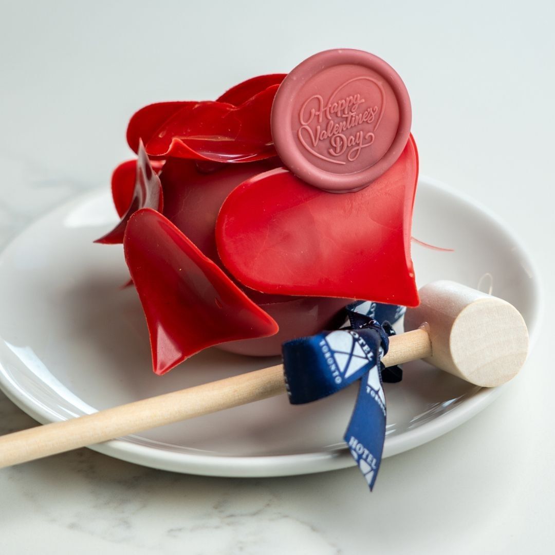 Red chocolate rose dessert with a wax seal on a white plate, beside a wooden mallet at Hotel X Toronto