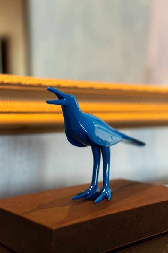 Blue Maria Mulata figurine with open beak on a brown base in front of a yellow-framed mirror.