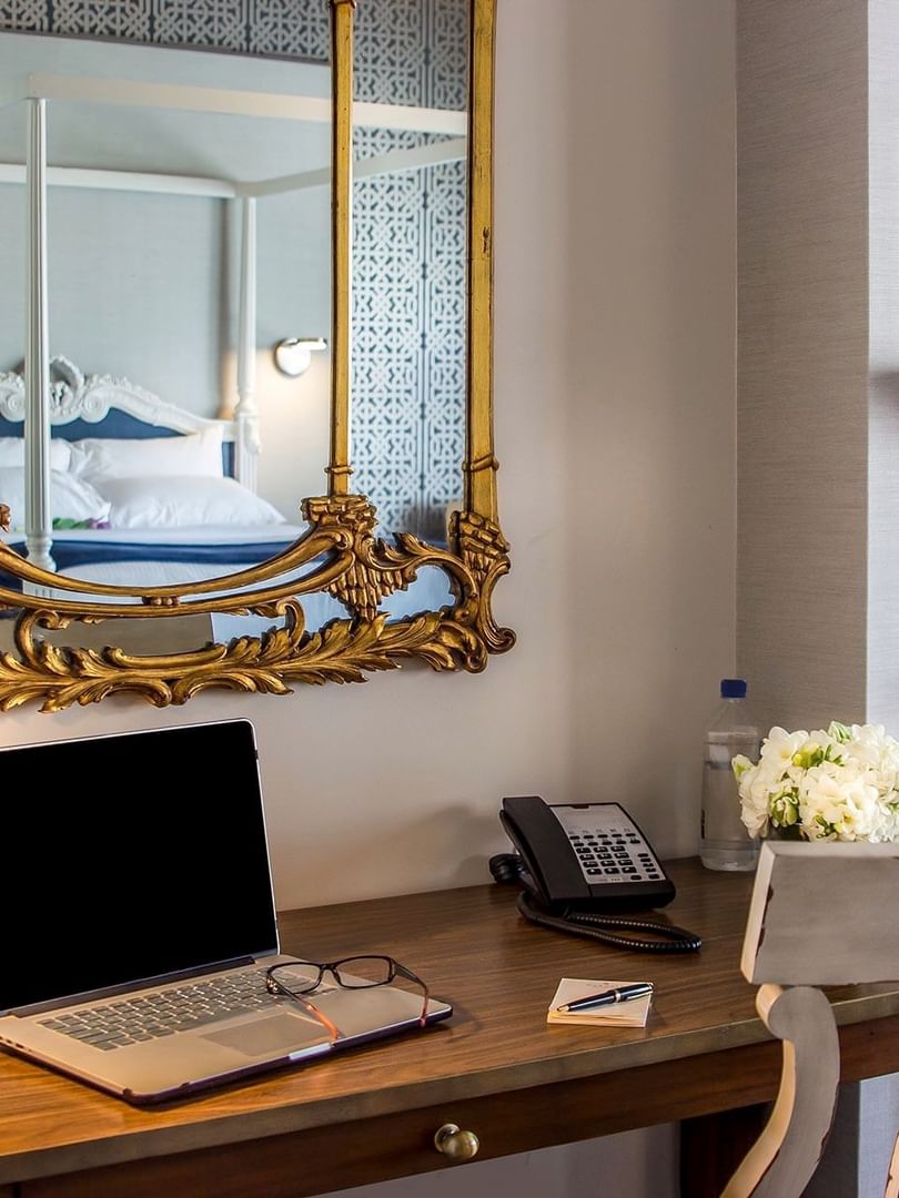 Laptop on a wooden desk by a gold mirror & white flowers under a grey wall in Loft Fireplace Suite at Warwick San Francisco