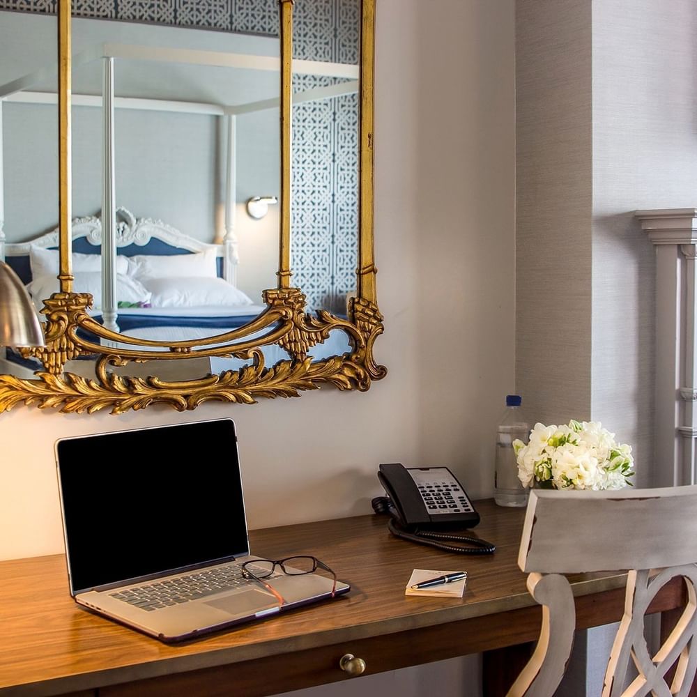 Laptop on a wooden desk by a gold mirror & white flowers under a grey wall in Loft Fireplace Suite at Warwick San Francisco