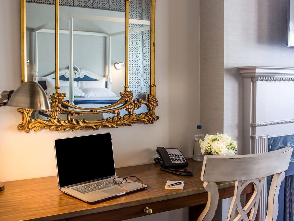 Laptop on a wooden desk by a gold mirror & white flowers under a grey wall in Loft Fireplace Suite at Warwick San Francisco