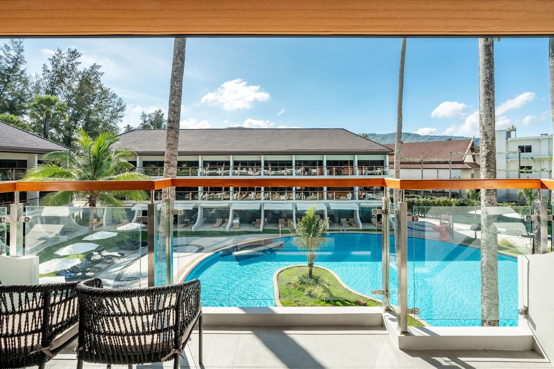 Balcony with views of a pool surrounded by palm trees and lounging areas in Deluxe Pool View at Amora Beach Resort Phuket