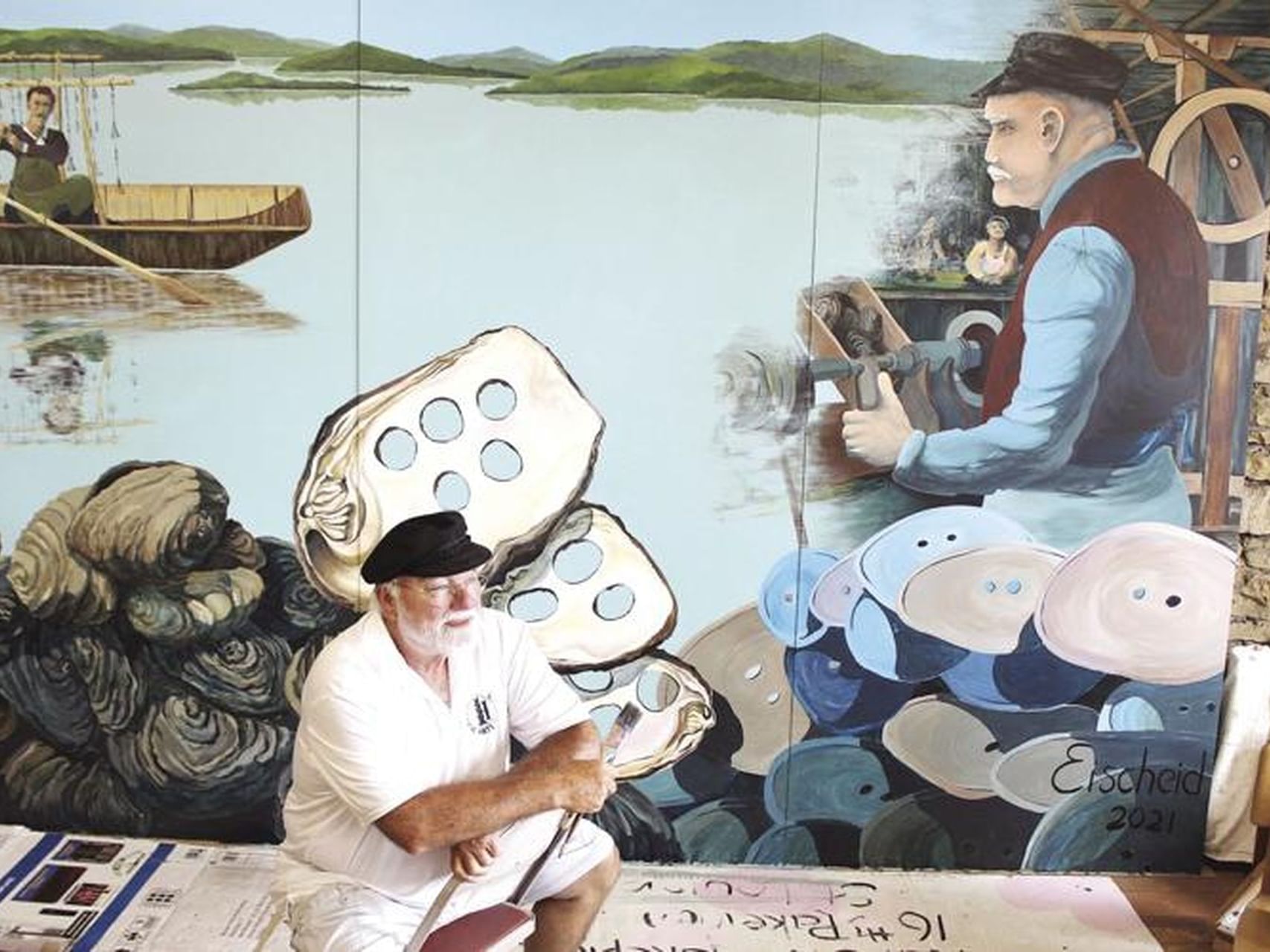 Artist seated in front of a mural depicting fishing and craftsmanship near Off Shore Resort, featuring Bellevue’s art culture