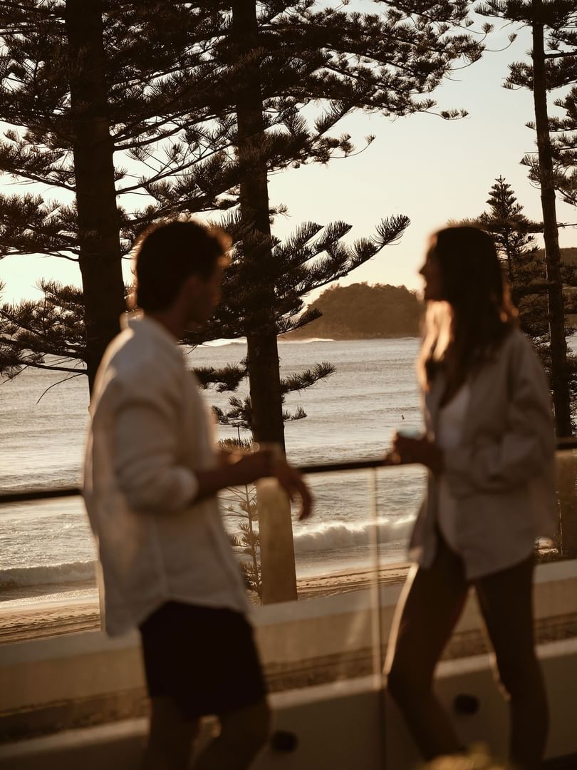 Silhouettes of a couple by a glass railing overlooking the sea at Elysium Manly, one of the best hotels in Manly